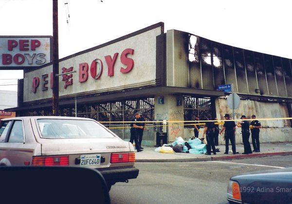 Police surrounded looted goods by burnt out store.